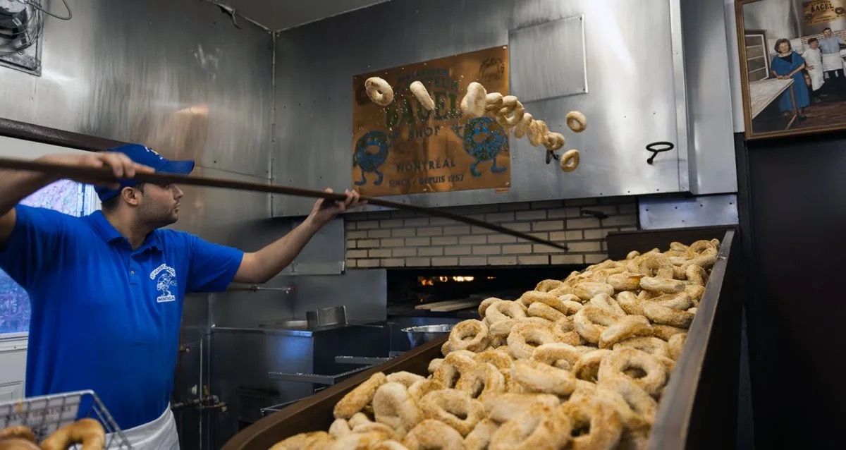 A St-Viateur baker flinging sesame bagels off a wooden peel by the wood-fired oven