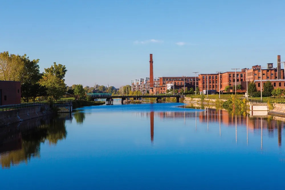 The Lachine Canal reflecting the sky, a brick smokestack and converted factory lofts along the far bank